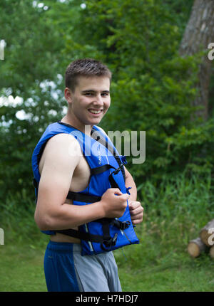 Young teen boy showing his prowess as he buckles up his water safety vest for lake activities. Clitherall Minnesota MN USA Stock Photo