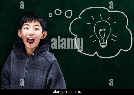Smart Asian boy with smart idea in classroom setting and chalkboard background. Stock Photo