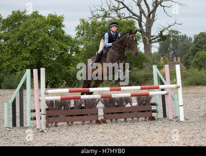teenage girl rider horse jumping jump mid air red white poles Stock Photo