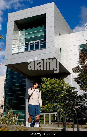 A male student walks with a cell phone in front of Duffield Hall, home of Cornell University's Nanoscale Science and Technology Stock Photo