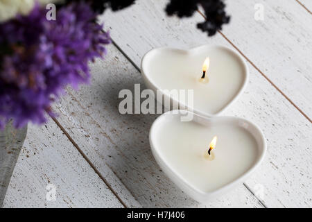 Two peaceful heart shaped candles on a white wood table Stock Photo