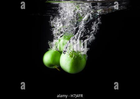 Three green apples splashing into water on black background Stock Photo