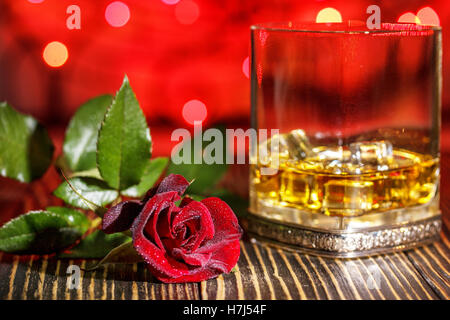Glass of scotch whiskey and ice ,  red rose  in   holiday colorful bokeh background on wooden table Stock Photo