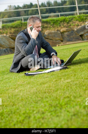 Businessman sitting in a park while using a laptop Stock Photo