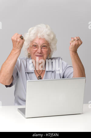 Elderly woman cheering while using a laptop Stock Photo