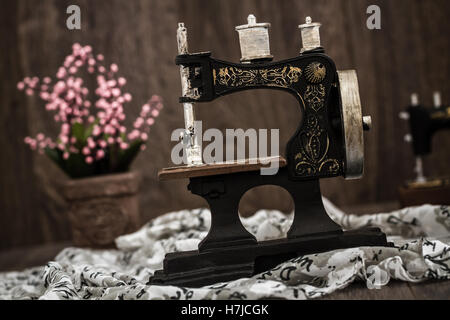 Small nostalgic decorative sewing machine on brown wooden background Stock Photo