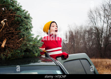 young boy with a chirstmas tree on the roof of the car Stock Photo