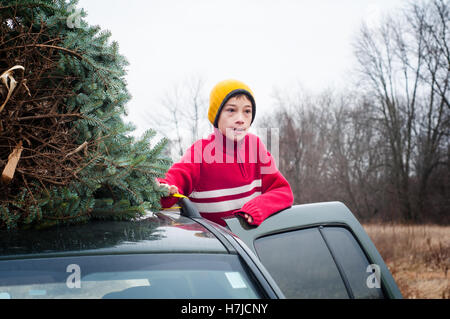 young boy with a chirstmas tree on the roof of the car Stock Photo
