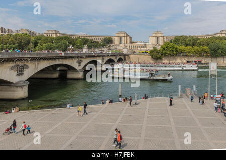 Tourist commercial boats going along the river Seine while people enjoy walking along it's banks Paris France Stock Photo