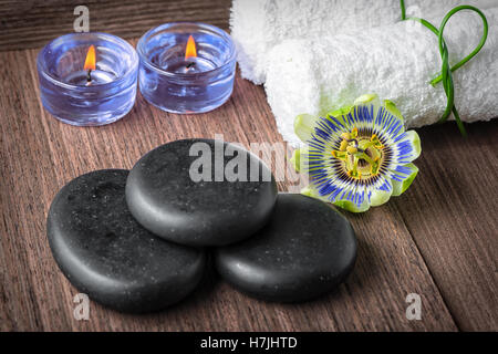 spa composition of passiflora flower, blue candles, black zen stones and white towels on wooden background, close up Stock Photo