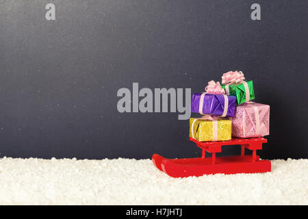 red festive sled with full gift boxes in snow on chalkboard background, winter holidays concept, copy space Stock Photo