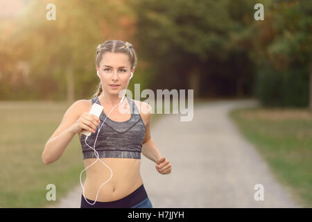 Woman listening to music on her earplugs and MP3 player while jogging along a country road in a healthy lifestyle concept