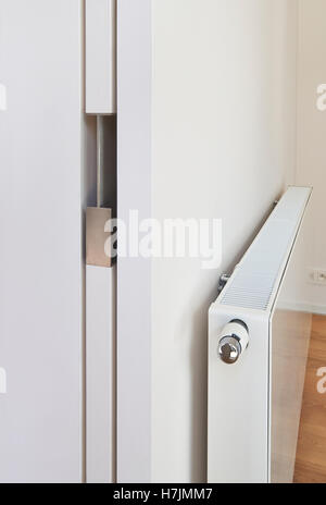 White radiator on wall with sliding door in an apartment with wooden floor Stock Photo