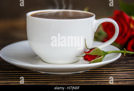 Cup of coffee and red roses on a wooden table in sunshine Stock Photo