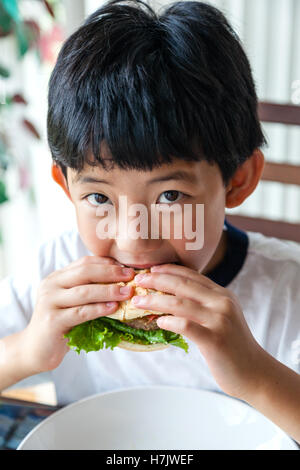 Asian boy taking a bite on his burger. Stock Photo