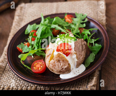 Baked potato filled with sour cream, arugula and tomatoes Stock Photo