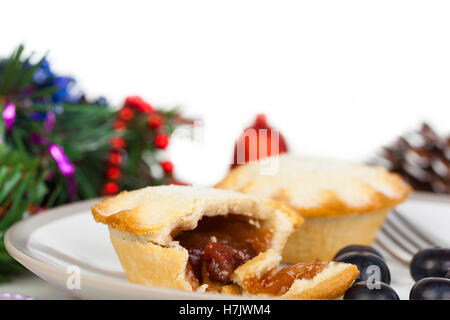 Part eaten mince pie with blueberries and christmas decorations against a white background Stock Photo