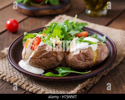 Baked potato filled with sour cream, arugula and tomatoes Stock Photo
