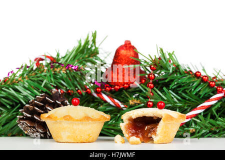 Two fresh mince pies in front of Christmas decorations against a white background Stock Photo
