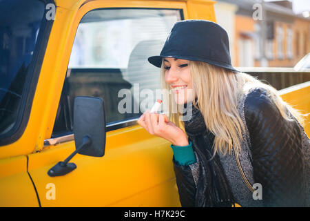 Sweet young woman applies red lipstick looking at the car mirror on a sunny autumn day Stock Photo