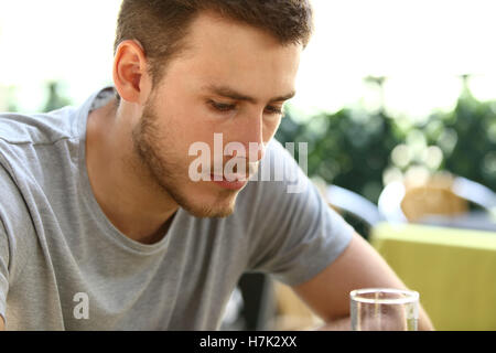 Portrait of a very sad single man sitting alone and drinking outside in a restaurant terrace Stock Photo