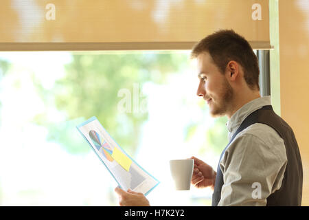 Side view of a business man reading growth statistics and drinking coffee near a window Stock Photo