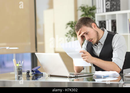 Sad businessman reading bad news in a letter sitting in a desk at office Stock Photo