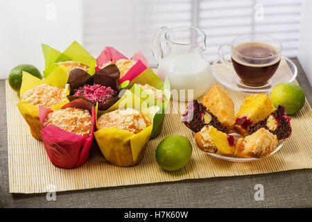 Color muffins in multi-colored paper, with milk, a cup of coffee and limes on mat from bamboo Stock Photo