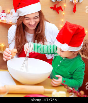 Mother with son baking Christmas cookies at home, with pleasure cooking together, wearing red Santa hats Stock Photo