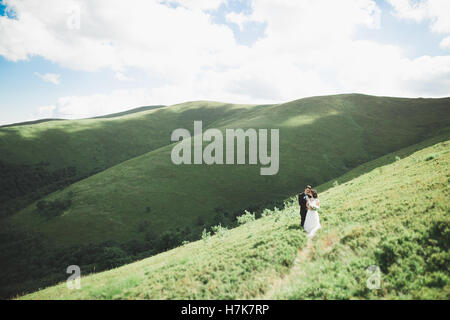 Beautiful fabulous happy bride and stylish groom posing on the background of the sunny stunning mountains Stock Photo