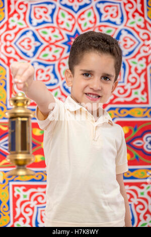 Happy Smiling Young Boy Celebrating Ramadan with Lantern over Festive Ramadan Curtain Stock Photo