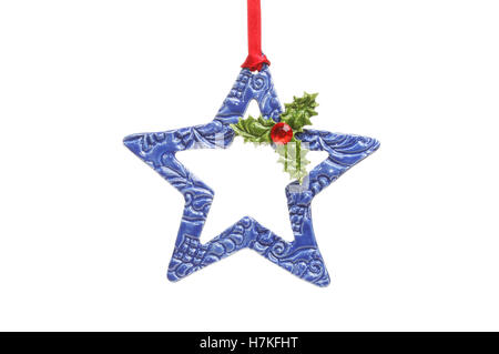 Blue ceramic Christmas star with ceramic Holly leaves and a jewel red berry hanging from red ribbon isolated against white Stock Photo