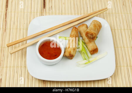 Spring rolls on a plate with sweet chilli dipping sauce and chopsticks on a bamboo matt Stock Photo