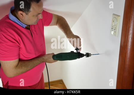 Man using electric drill to make a hole in a wall at home Stock Photo