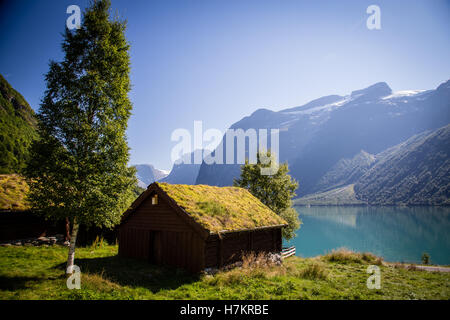 A view across Lovatnet Lake, a traditional Norwegian house sits in the foreground topped with sod roof. Stock Photo