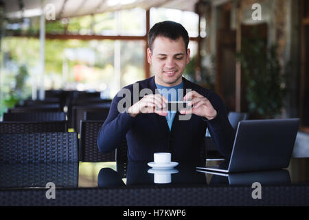 Young student man taking photo of a coffee cup and using laptop in canteen at the university or street cafe Stock Photo