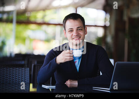 Handsome young man working on laptop and smiling while enjoying coffee in cafe Stock Photo