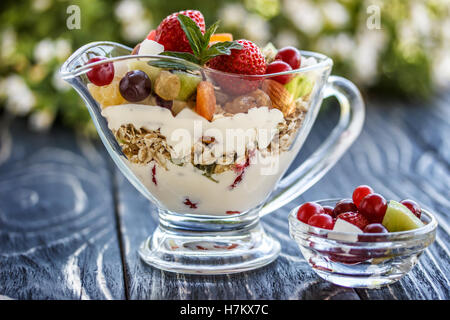 Fruit salad closeup with berries, yogurt and granola in a glass bowl on an old wooden board
