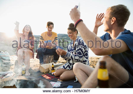 Young couples gesturing playing cards at summer beach campsite