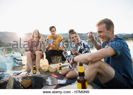 Young couples gesturing playing cards at summer beach campsite
