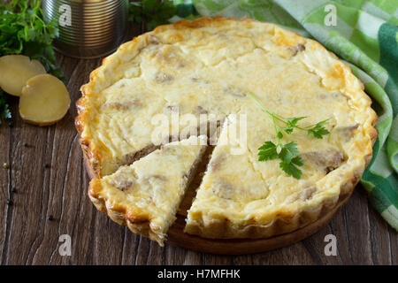 A classic quiche Lorraine pie with potatoes, meat and cheese in a baking dish on a table in a rustic style. Stock Photo