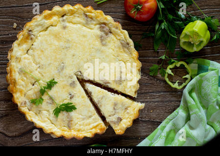 A classic quiche Lorraine pie with potatoes, meat and cheese in a baking dish on a table in a rustic style. Stock Photo