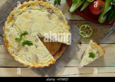 A classic quiche Lorraine pie with potatoes, meat and cheese in a baking dish on a table in a rustic style. Stock Photo