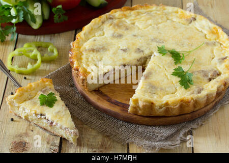 A classic quiche Lorraine pie with potatoes, meat and cheese in a baking dish on a table in a rustic style. Stock Photo