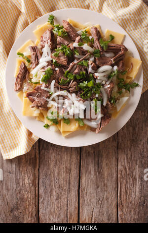 Beshbarmak dish: noodles with lamb and onion close-up on a plate on the table. Vertical top view Stock Photo