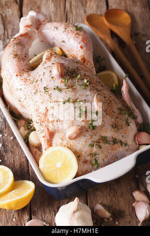 raw whole chicken marinated with garlic, thyme and spices close up in baking dish on the table. Vertical Stock Photo