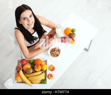 Beautiful women exists with pure skin on her face sitting at a table and eat breakfast. Asian woman eating healthy food at breakfast. Fruit, cereal and milk. Unusual view, top view, selective focus Stock Photo