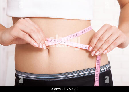 sport, fitness and diet concept - closeup of trained belly with measuring tape Stock Photo