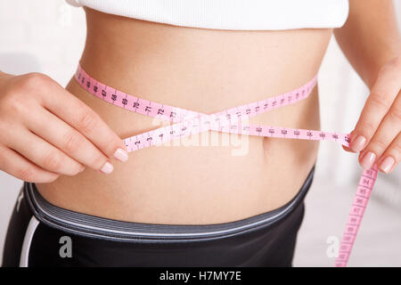 sport, fitness and diet concept - closeup of trained belly with measuring tape Stock Photo