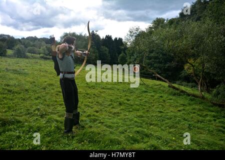 Young medieval archer of the side, aims with arrow and curve at straw disc in green nature Stock Photo